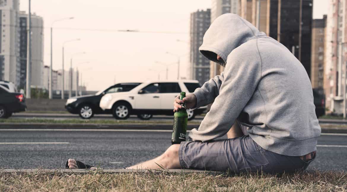 The Dangers of Alcohol Detox Symptoms, a man sitting on the edge of the road with a liquor bottle